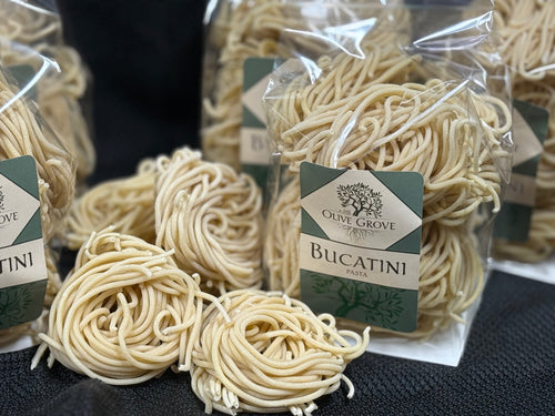 Packages of Olive Grove Bucatini pasta on a black surface